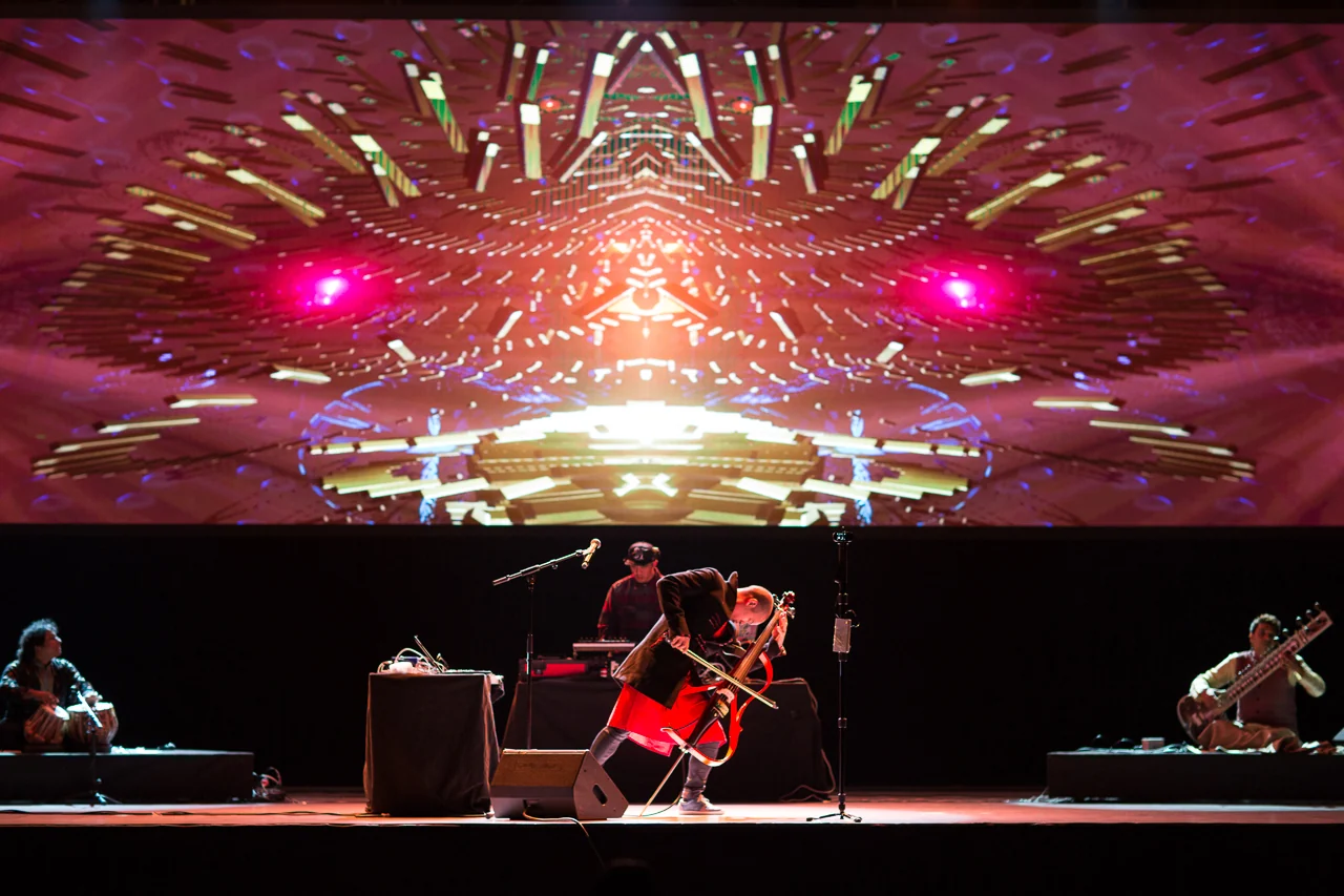 The TEKTONIK ensemble on a wide stage beneath a vast projected mandala, Dana Leong bowing centre with tabla and sitar either side