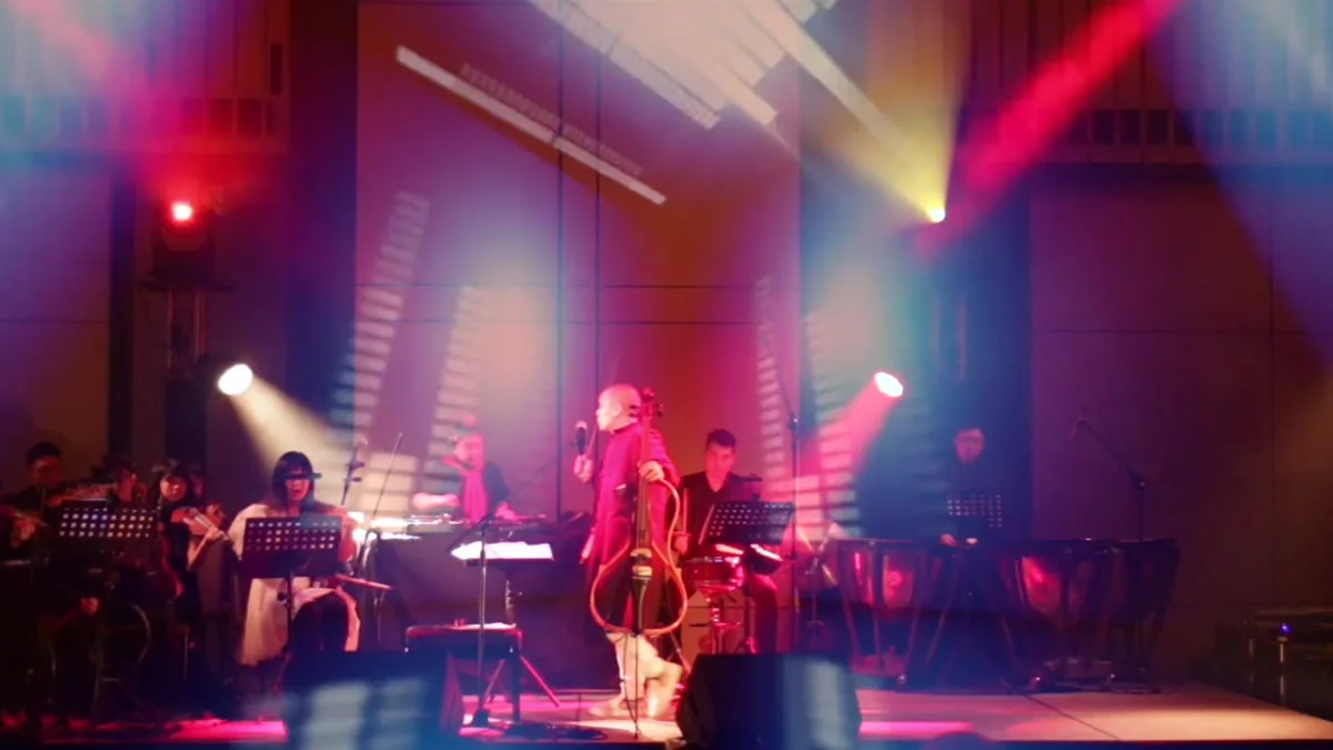 The TEKTONIK Electronic Symphony on stage under pink and blue beams, Dana Leong centre with his orange electric cello